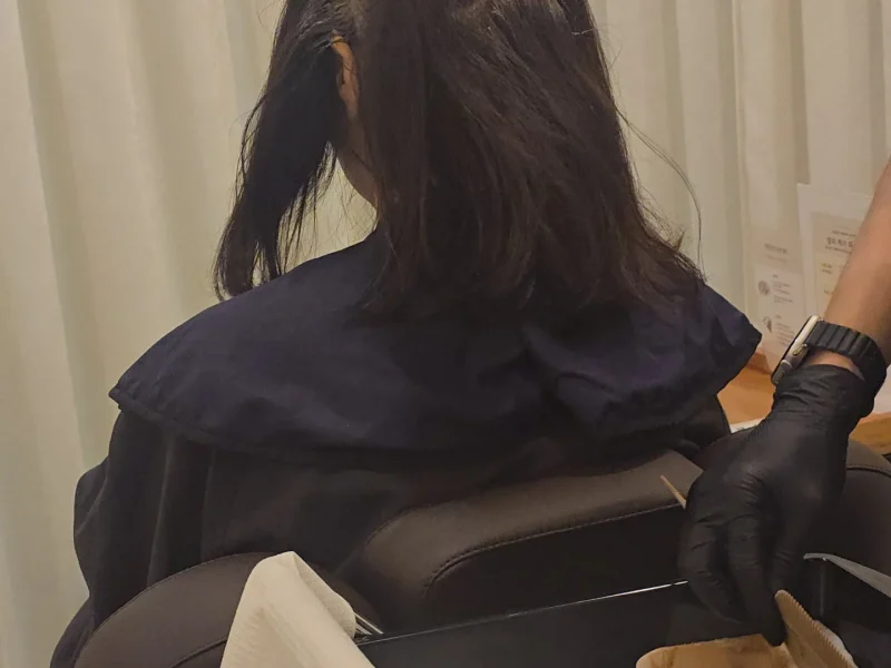 의자에 앉은 고객의 모발에 컬러 제품을 도포하는 스태프